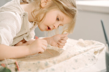 Obraz na płótnie Canvas Little girl makes a clay plate and decorates it