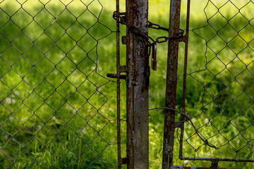ein altes rostiges Eisentor ist mit einer Kette verschlossen und versperrt den Zutritt zur Wiese
