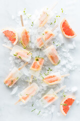 Refreshing grapefruit thyme popsicles scattered around on a bed of ice.