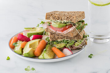 A healthy whole grain sandwich with fresh cut vegetables and a glass of water.