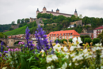 Marienberg Fortress upon a vineyard hill above the Old Bridge and Main river seen from the other site of the river through colorful blooming summer or spring flowers
