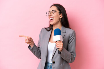 Young caucasian tv presenter woman isolated on pink background pointing finger to the side and presenting a product