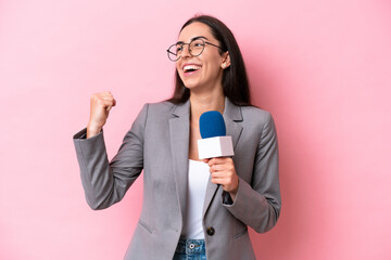 Young caucasian tv presenter woman isolated on pink background celebrating a victory