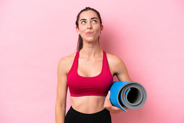 Young sport caucasian woman going to yoga classes while holding a mat isolated on pink background...