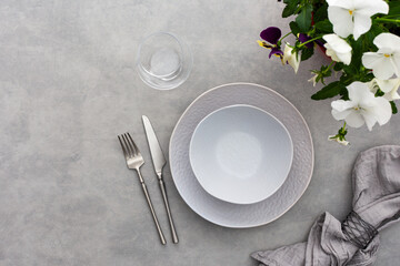 Table setting, empty plate with napkin and cutlery on the on the gray background, top view of the served table decorated with pansies flowers