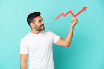 Young handsome caucasian man isolated on blue background holding a catching a rising arrow with happy expression