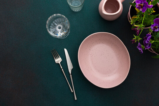 Table setting, empty pink plate and cutlery on a green background, top view of the served table decorated with pansies flowers