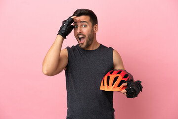 Young cyclist man isolated on pink background doing surprise gesture while looking to the side - obrazy, fototapety, plakaty