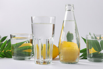Distortion of an object through transparent vessels filled with water. Distorted lemons and green leaves lie behind glass vessels