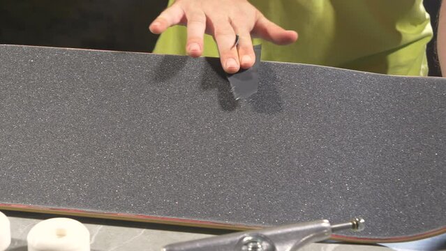 CLOSE UP: Young man softening the cut edges of griptape on brand new skateboard with leftover scraps. Unrecognizable male person applies finishing touches to a new skateboard deck to get a smooth edge