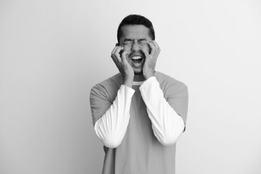 Adult Asian man screaming with both hand scratching his face
