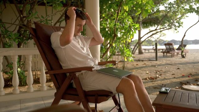 Young caucasian man starting typing on laptop and surfing Internet. Some work on vacation, while resting in beach chair.