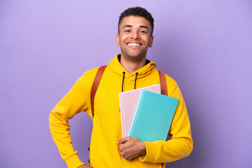 Young student Brazilian man isolated on purple background posing with arms at hip and smiling - obrazy, fototapety, plakaty