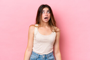 Young caucasian woman isolated on pink background looking up and with surprised expression