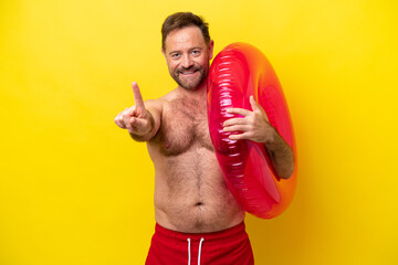 Middle age caucasian man holding inflatable donut isolated on yellow background showing and lifting a finger