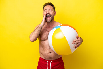 Middle age caucasian man holding beach ball isolated on yellow background shouting with mouth wide open