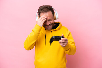 Middle age man playing with a video game controller isolated on pink background laughing