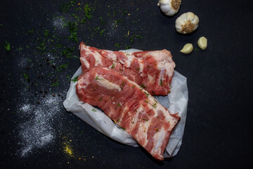 Raw pork meat on a black background from above, in the background garlic and onions. The meat is prepared for marinating and frying