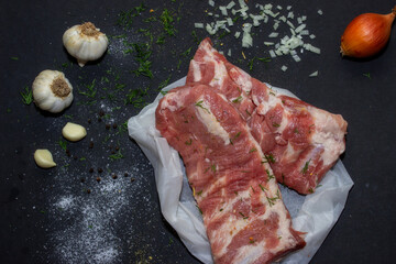 Raw pork meat on a black background from above, in the background garlic and onions. The meat is prepared for marinating and frying