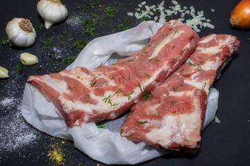 Raw pork meat on a black background from above, in the background garlic and onions. The meat is prepared for marinating and frying