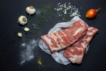 Raw pork meat on a black background from above, in the background garlic and onions. The meat is prepared for marinating and frying