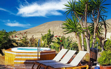 Schöne Oase der Ruhe, leere Gartenterrasse, Whirlpool, Liegestühle, Palmen, trockener, karger Landschaftshintergrund - Strand von Sotavento, Fuerteventura