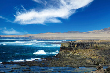 Beautiful lonely wild rough south-east coast, jagged rocks, strong waves, dry arid sand dunes, steep cliffs, clear blue sky - Jandia national Park, Fuerteventura