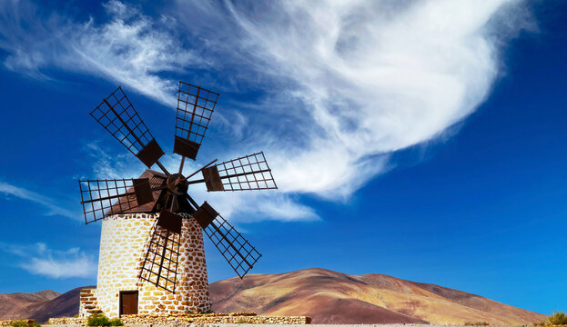 Isolated traditional round spanisch stone windmill (Molino de Tefia), dry arid hilly landscape, blue sky white cloud - Fuerteventura, Canary Islands