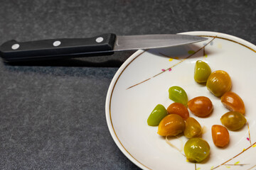 Multi-colored cloves of peeled pickled garlic for seasoning on a porcelain plate with a kitchen vegetable knife with copy space.