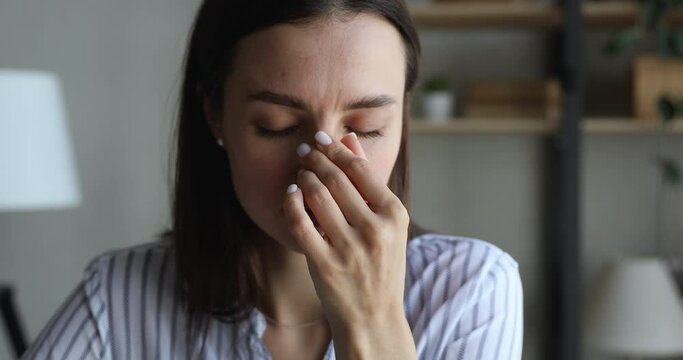 Close up view face of exhausted female employee feels unhealthy massage nose bridge touches temples suffers from migraine. Throbbing headache, high blood pressure, hypertension need rest, meds concept