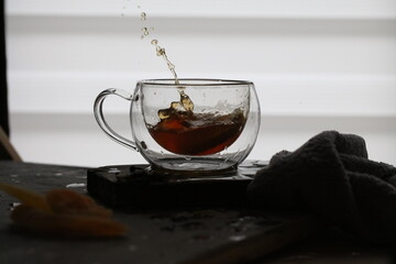 Transparent double walled tea cup with black tea and a splashing lemon piece