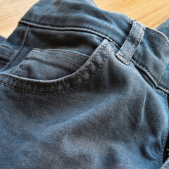 Close up detail of pocket of light blue jeans, on wooden floor