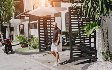 Young businessman walking out of his modern home with garage and car
