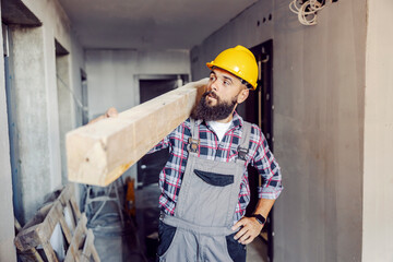 A strong worker holding wooden beam on the shoulder and relocating it in a building in construction...