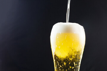 pouring beer into a takan on a dark background. beer foam flows down the walls of the glass