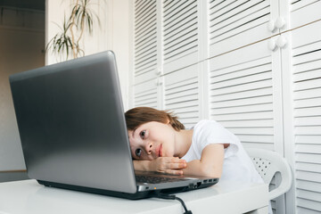 Boy lies at the table, looks at the computer screen. Tired pupil. Difficult, boring, uninterested...