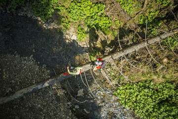 Naklejka premium Hiking Couple Crossing River Walking Along Fallen Tree Aerial View.
