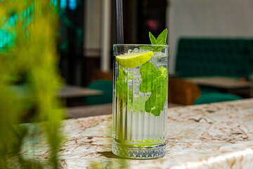 Mojito rum alcoholic cocktail served in a highball glass with ice cubes garnished with lemon and mint at the bar