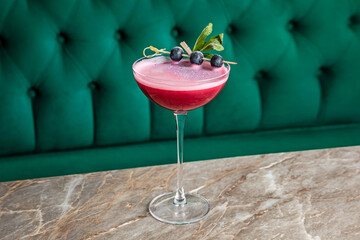 A pink sour alcoholic cocktail with great bilberry served in a coupe glass