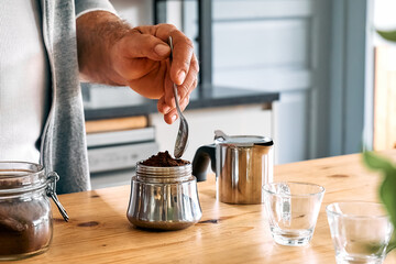 Fototapeta na wymiar Man preparing classic Italian coffee in the mocha in the kitchen, filling funnel of a moka pot with ground coffee. Coffee brake. Morning habit.