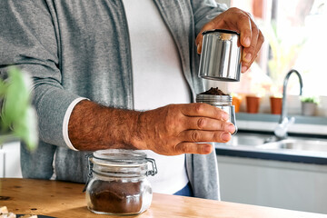 Man preparing classic Italian coffee in the mocha in the kitchen. Pouring coffee from moka pot into small glass coffee cup. Coffee brake. Morning habit.