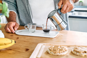 Man preparing classic Italian coffee in the mocha in the kitchen. Pouring coffee from moka pot into small glass coffee cup. Coffee brake. Morning habit.