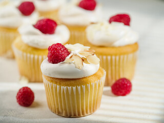 Buttercream muffins garnished with raspberries and almonds on a white background. Confectionery,...