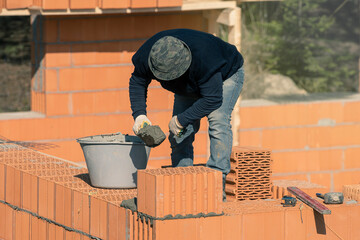 Builder applies cement for laying bricks on the wall. Bricklaying. Bricklayer builder, private master. Construction of a cottage, a country house. - obrazy, fototapety, plakaty