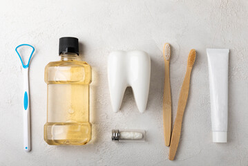 Eco bamboo toothbrushes, tongue cleaner, floss, tooth mockup, tube of toothpaste and mouthwash on gray background with copy space. Flat lay. Dental hygiene. Oral care product set. Dentist concept