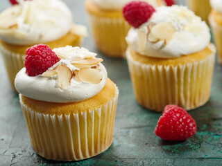 Muffins with cream, fresh raspberries, decorated with pieces of nuts. Isolated on a dark green background. Festive mood, sweet food, children, youth culture. Close-up.