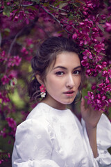 Fototapeta premium portrait sexy young woman in a white dress and purple tights stands by the blooming purple cherry trees in spring.