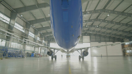 Airplane in hangar, rear view of aircraft and light from windows. Large passenger aircraft in a hangar on service maintenance