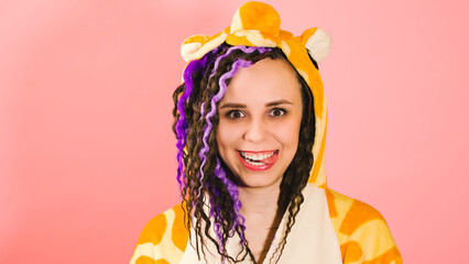 Young cute woman with dreadlocks in kigurumi looking at camera and showing tongue. Funny playful...
