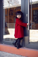 Korean girl in a red coat and beret stands on the street against at the glass doors of the store in autumn